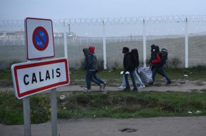 Migrants, carrying their luggage, walk past a Calais city limit sign as they head towards an official meeting point set by French authorities as part of the full evacuation of the Calais "Jungle" camp, in Calais, northern France, on October 24, 2016. French authorities began on October 24, 2016 moving thousands of people out of the notorious Calais Jungle before demolishing the camp that has served as a launchpad for attempts to sneak into Britain. Migrants lugging meagre belongings boarded buses taking them away from Calais' "Jungle" under a French plan to raze the notorious camp and symbol of Europe's refugee crisis. / AFP PHOTO / FRANCOIS LO PRESTI